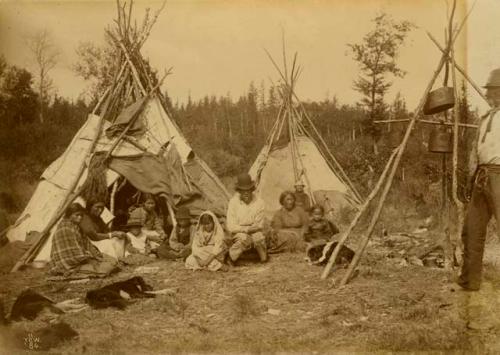 Cree men, women and children in front of canvas and birch bark covered teepees