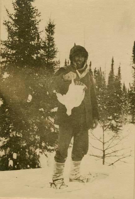 Cree man wearing snow shoes and holding up a white bird