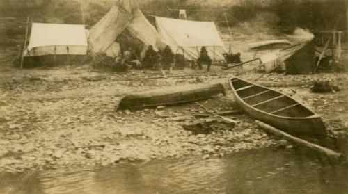 Group of Cree people in front of tents on lake shore
