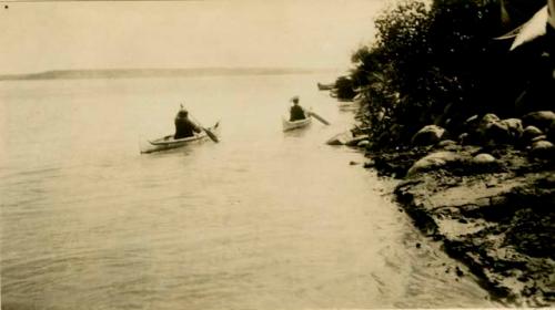 Two Cree people paddling bark canoes