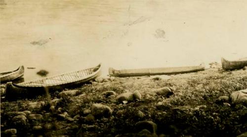 Four bark canoes pulled up on shore of lake