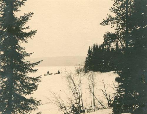 Two people leading loaded dog sleds across snow. Ashuapmouchan river