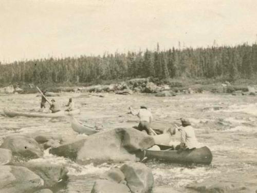 Five men travelling down white water section of river in canoes