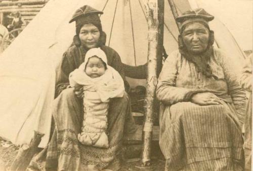 Two women seated on chairs in front of tent.