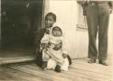 Girl in western dress holding baby on her lap, sitting on porch