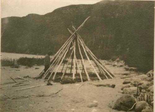 Tepee frame with man standing by it.