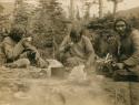 Three Naskapi men sitting around a campfire eating and drinking