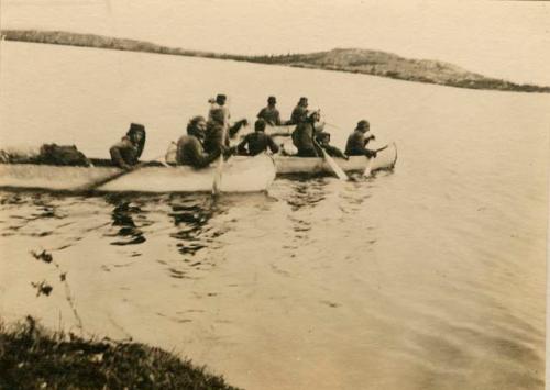 Three canoes in water, loaded with paddlers and cargo