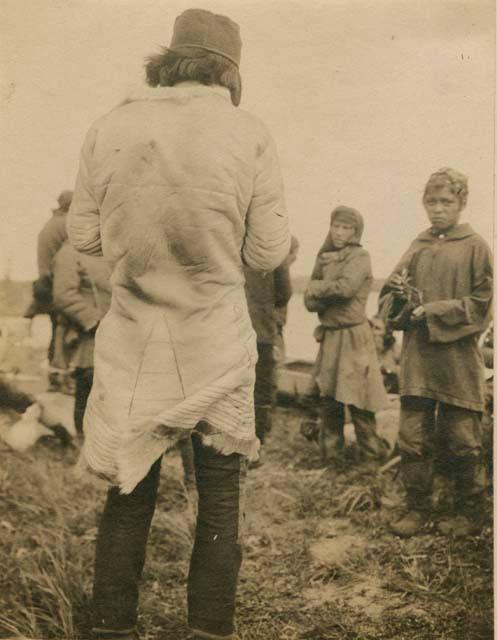 Small group of people, man with back to camera wearing traditional coat.