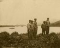 Group of Aleut men standing near coast