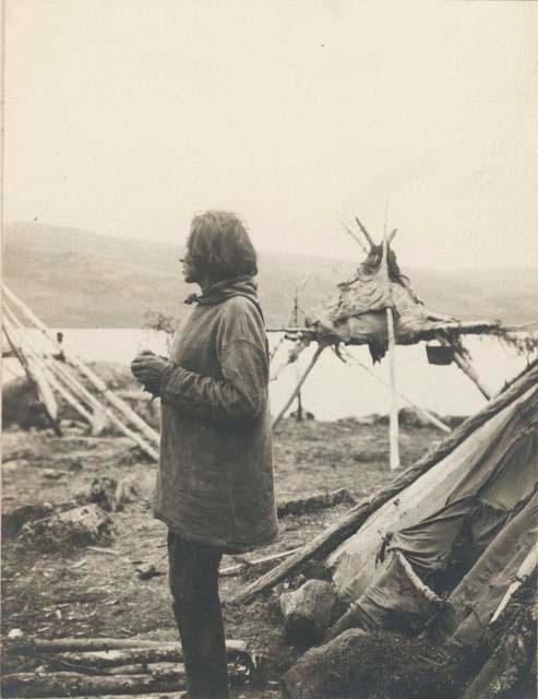 Profile of man, platform in background and edge of tepee to left.