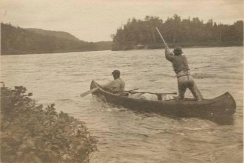 Two men in birchbark canoe, one paddling, one poling