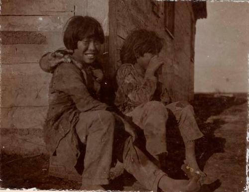 Two boys sitting outside of wooden cabin