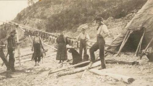 Four men and one woman standing in front of a rack strung with fish