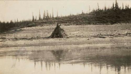 View of Spruce bough tepee on river bank.