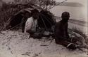 Two Aboriginal men and one young boy seated on sand before a small shelter