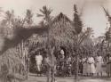 Large group of standing in front of house, palms in foreground