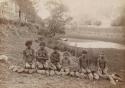 Three Aboriginal women and three Aboriginal children photographed in bush kneeling behind 19 fish