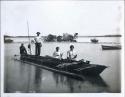 Two Aboriginal women, three men, and one white dog photographed in an outrigger canoe on the water