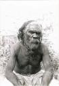 Older Aboriginal man in close-up, sitting on ground in scrubland