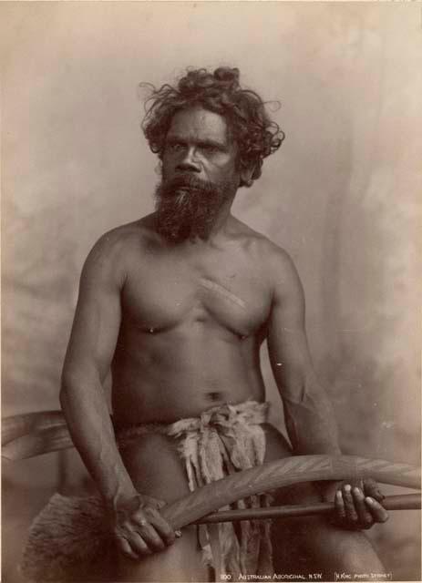 Studio portrait of an Aboriginal man holding a boomerang and a club