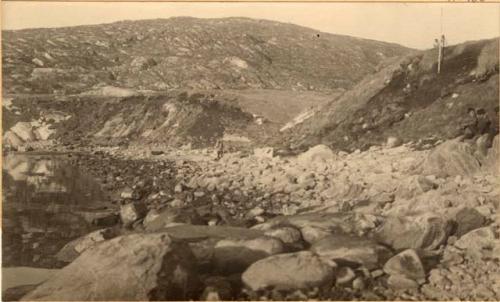 Sermermiut. Men Excavating in the hillside above rocky beach.