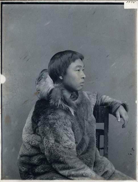 Inuit boy wearing fur parka, sitting, profile