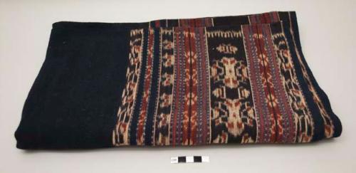 Woven textile; black or dark indigo center with bands of dark red, ecru and blue ikat at both sides.