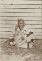Haida woman sitting on the ground and holding a cane