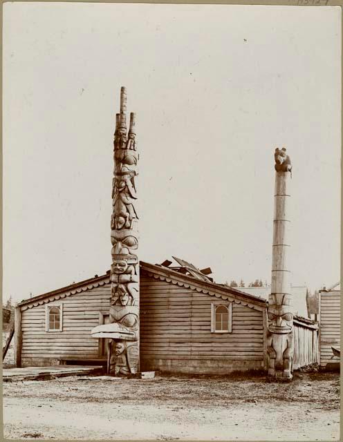 Two totem poles in front of dwelling, Massett