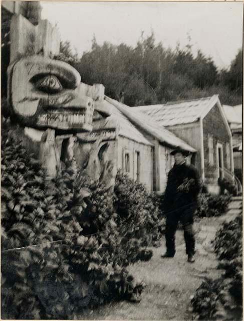 Man walking towards totem poles at entrance to house