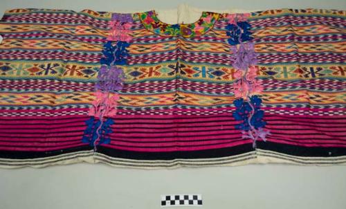 Huipil, large women's shirt, white cotton with a decorated top half showing horiztonal bands of black and white ikat, bands of multicolored geometric designs, floral embroidery at neck and in a vertical band on either side of shirt