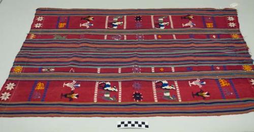 Tzute, women's multipurpose headcloth, two pieces sewn together, red with multicolored stripes in the middle and on the edges, multicolored animal, floral, human, and geometric images.