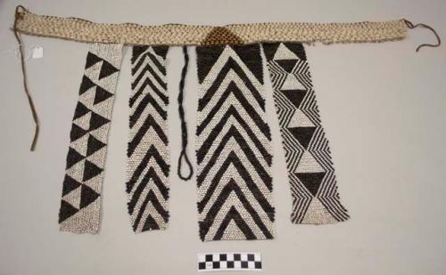Beaded cache sex; waist band of ostrich eggshell beads with central triangle pattern of metal beads; four dangling panels of different widths; each panel with black, white and dark blue beads in different geometric patterns