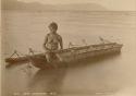 Aboriginal Woman sitting on canoe in water, holding a wooden paddle