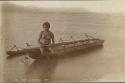 Aboriginal Woman sitting on canoe in water, holding a wooden paddle