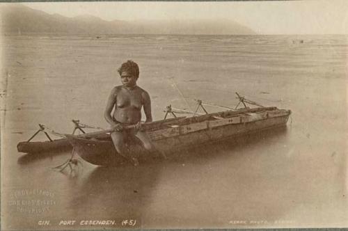 Aboriginal Woman sitting on canoe in water, holding a wooden paddle