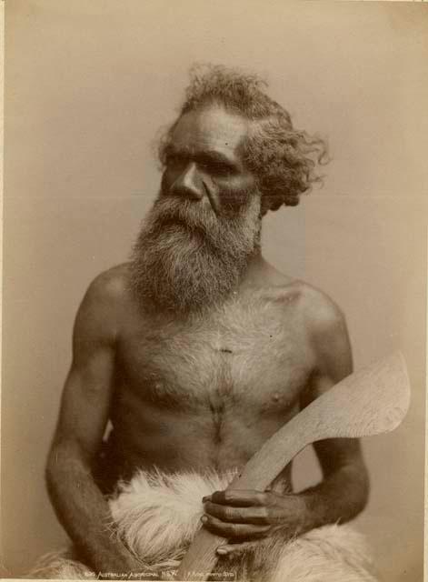 Studio portrait of an Aboriginal man holding a hook-necked boomerang or club