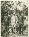 Three Aboriginal men photographed in the bush holding spears and spear throwers; the man in center is painted with white ochre