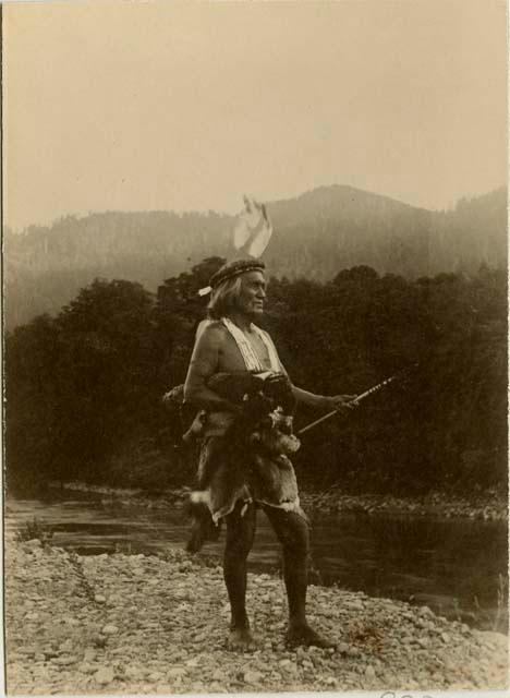 Yurok man wearing a feather headdress and holding arrows