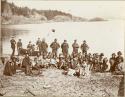 About fifty Nootka people sitting on the shore. Ten sailors in background