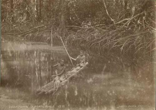 Two Cooktown Aboriginal boys floating on a log raft in the water near a mangrove bank