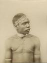 Studio portrait of an Aboriginal man wearing a reed necklace, tooth headband, twine armbands and twine cords across chest