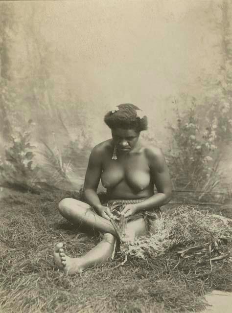 A native woman in a studio staged scene weaving plant fiber