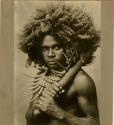 Studio portrait of a young Fijian man wearing a necklace of tusks and holding a club
