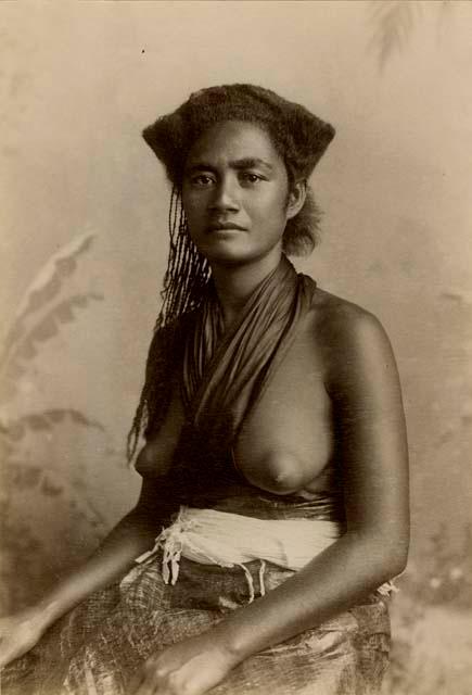 Studio portrait of a Fijian woman wearing fabric around her waist and neck, with bare breasts
