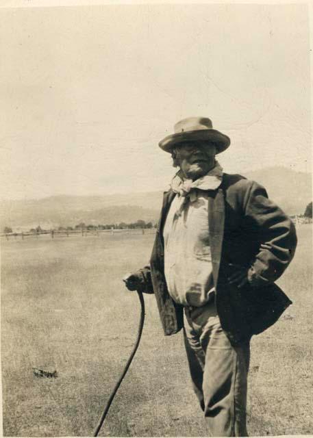 Man with hat, cane, jacket, kerchief in open field