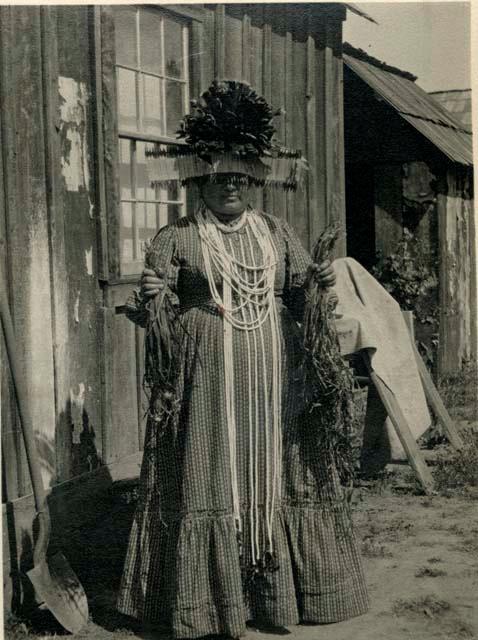 Mary in woman's dance outfit with ceremonial headdress, holding plants