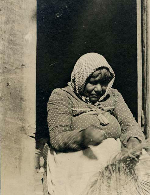 Pomo weaver in doorway weaving basket.