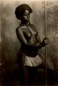 Studio portrait of a Fijian woman holding a spear, carrying a basket, and wearing a grass skirt
